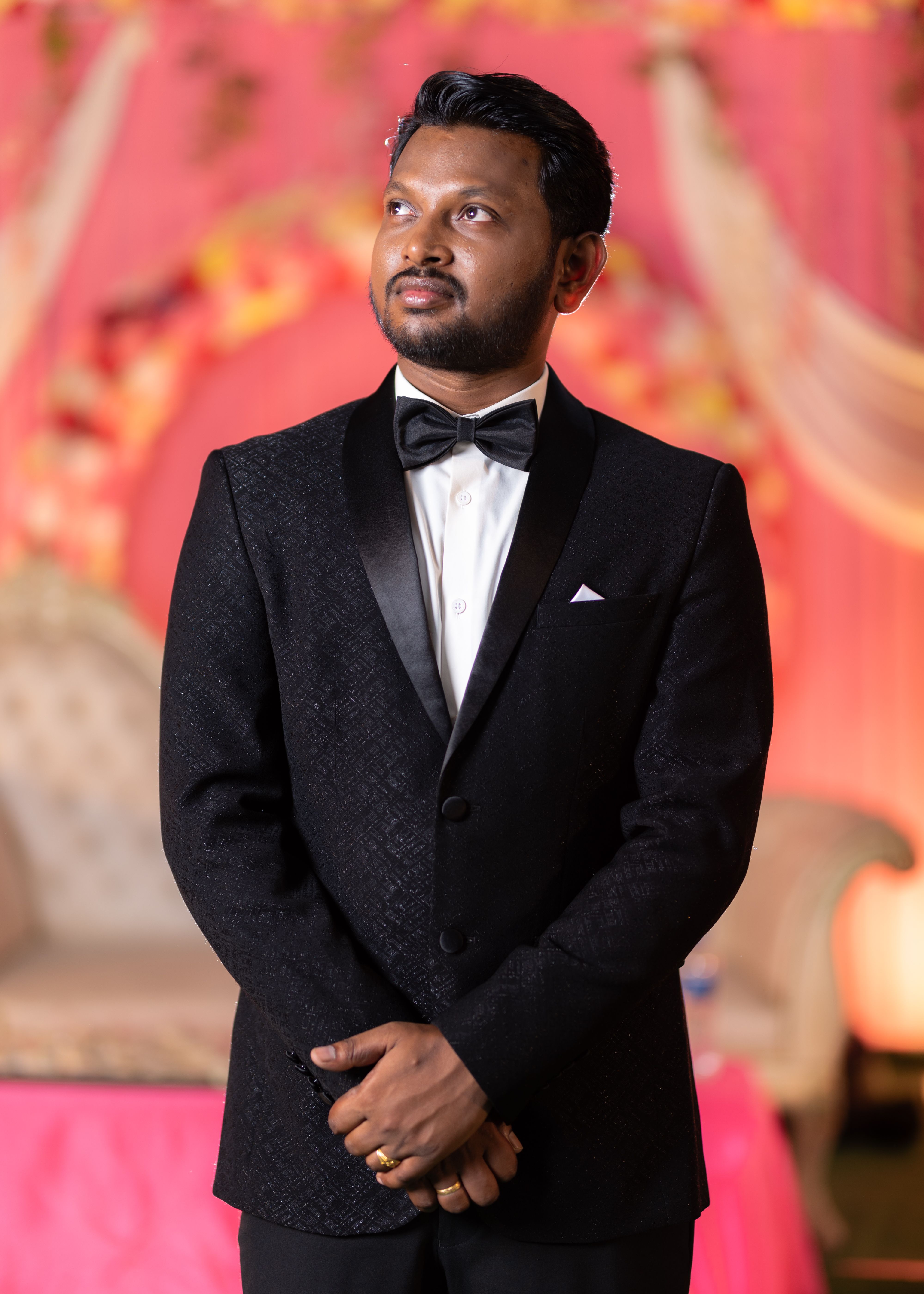 A groom in a sophisticated tuxedo poses indoors at a Kerala wedding.