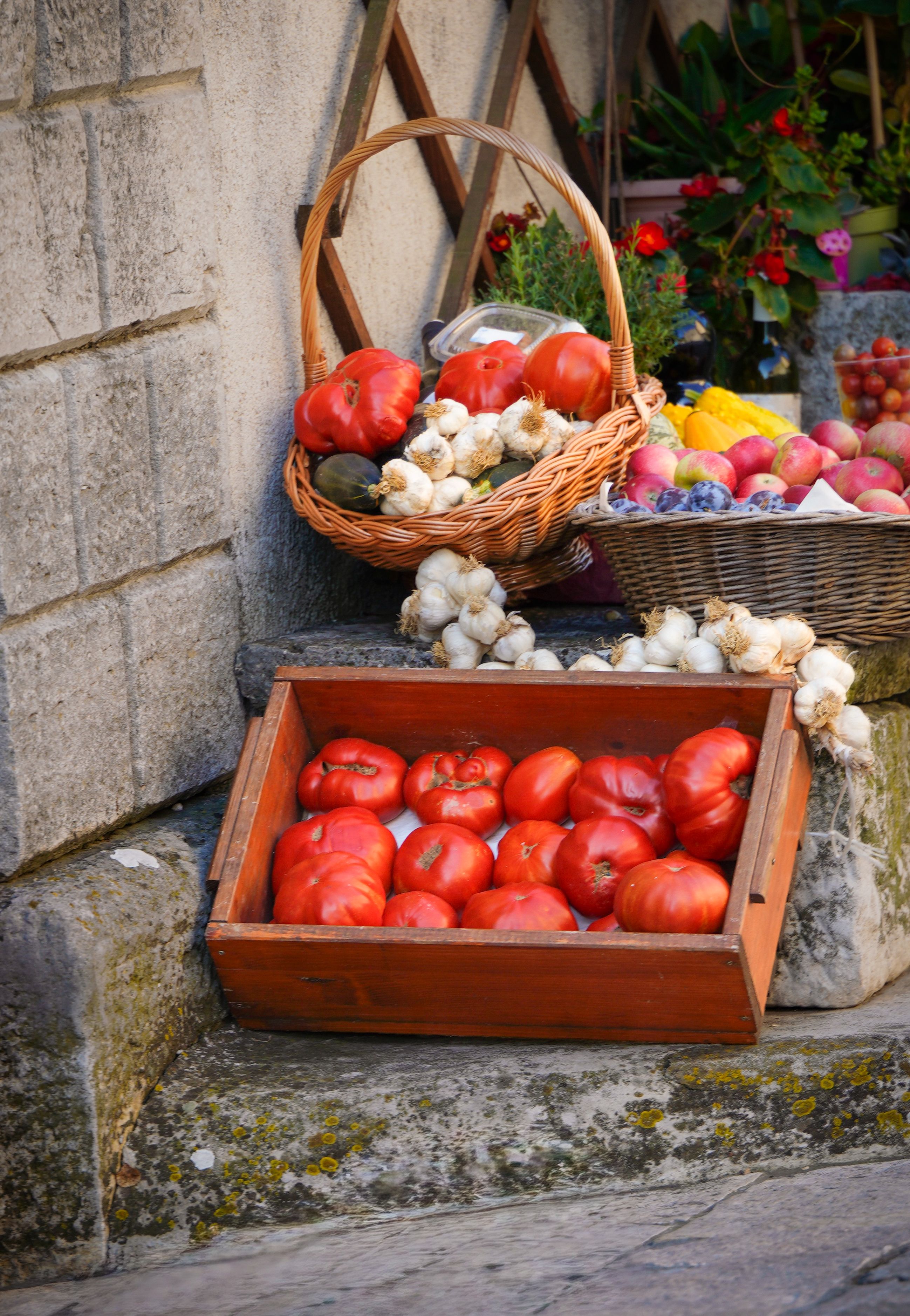 Cageot de tomates cœur-de-bœuf, tresses d'ail et corbeilles de fruits sur des marches en pierre