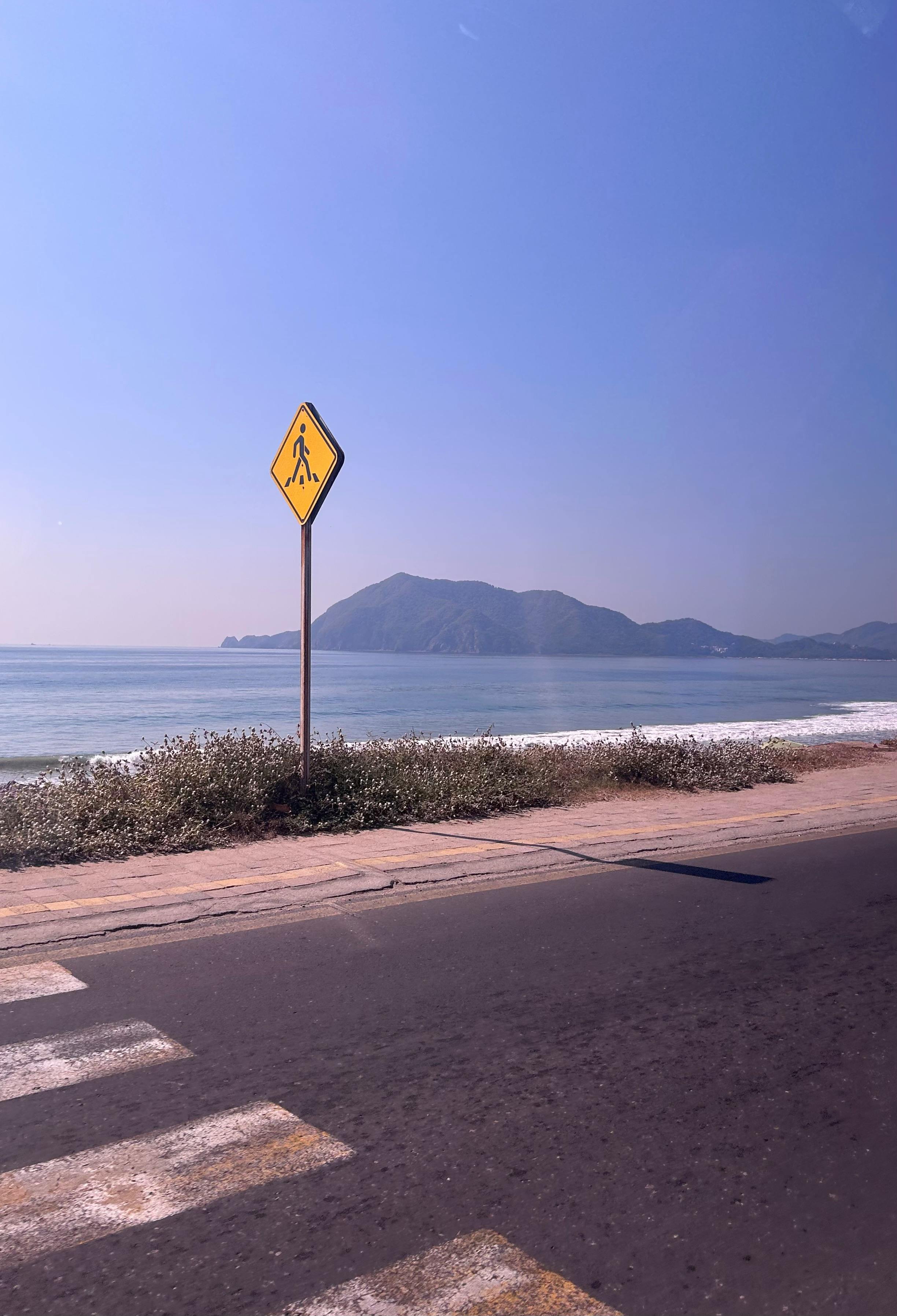 A tranquil view of a coastal road in Manzanillo, Mexico, with a pedestrian sign and mountainous backdrop.