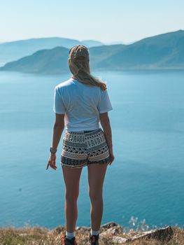 A woman in shorts and a cap enjoys a breathtaking mountain lake view.