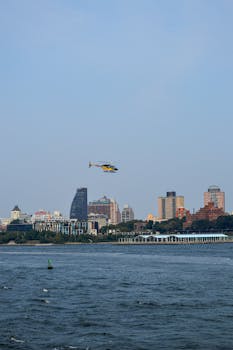 A helicopter soars above the Hudson River with the New York City skyline in the background.