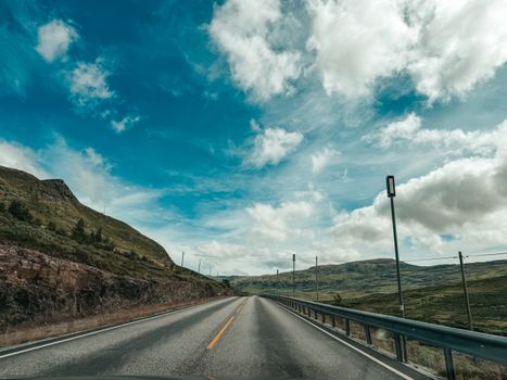 Open road through rugged mountains under a bright blue sky with clouds.