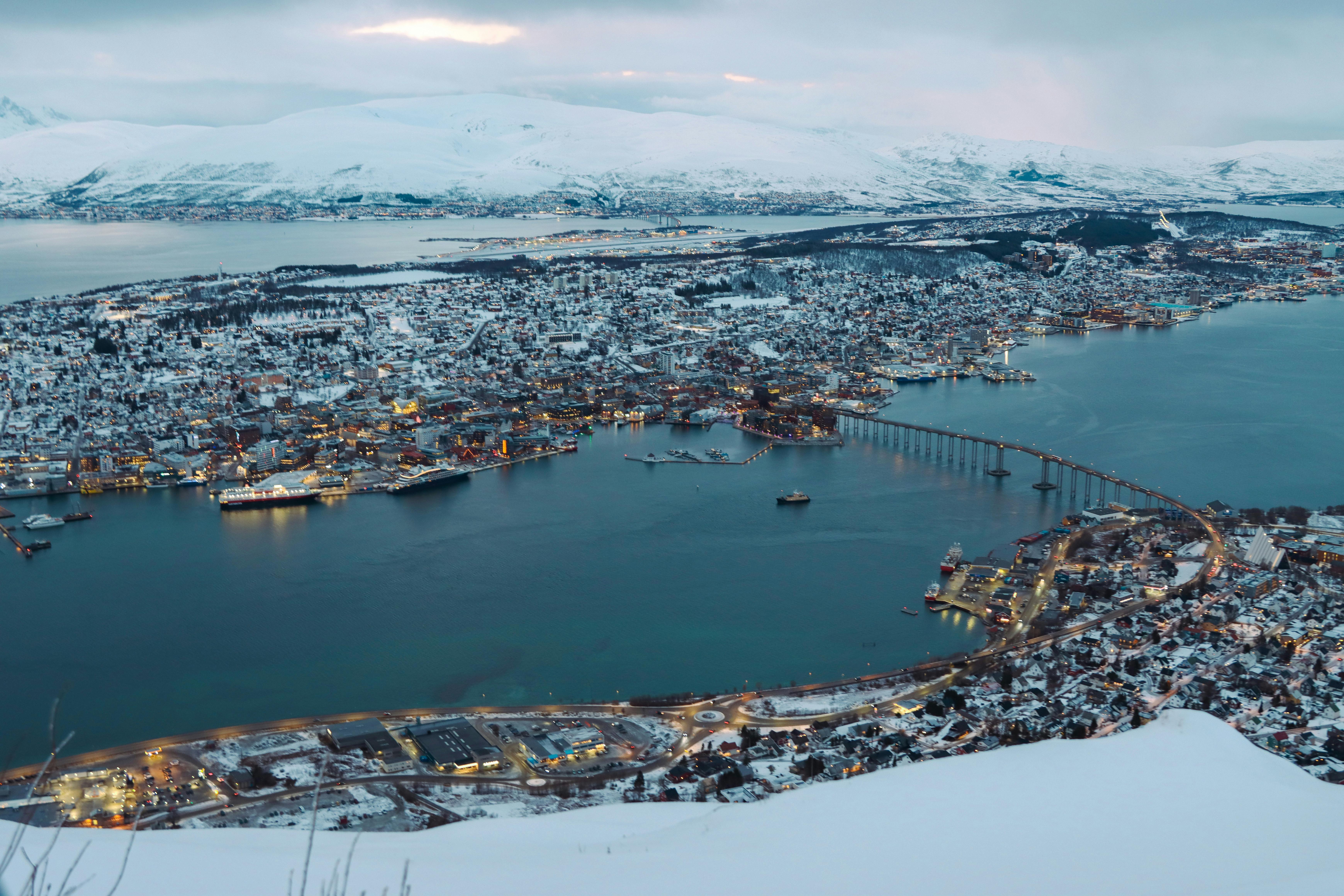 Stunning aerial cityscape of Tromsø, Norway blanketed in snow, showcasing bridges and coastline.