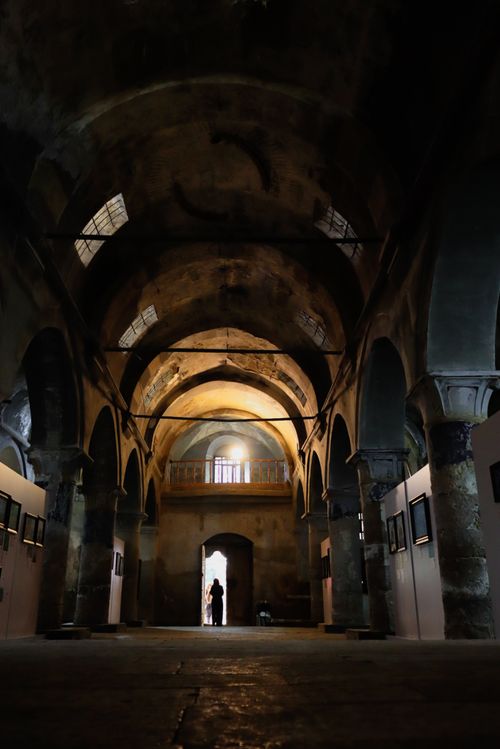 Free Dimly lit historic hallway with arches and a solitary figure in the distance. Stock Photo