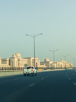 A road view with Middle Eastern architecture under a clear sky, featuring modern infrastructure and vehicles.
