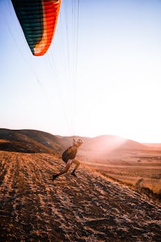 A paraglider launching from a hill ridge at sunset with colorful chute in scenic landscape.