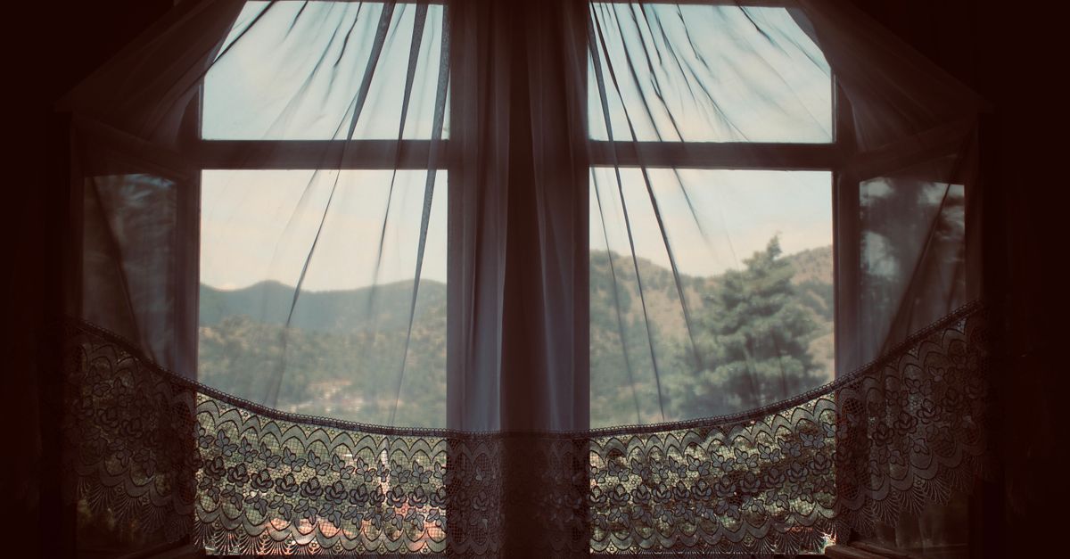 Serene landscape through a vintage window with lace curtains, capturing the peaceful outdoors.