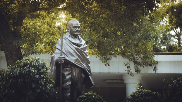 Bronze statue of Mahatma Gandhi surrounded by greenery in a serene garden in Delhi, India.