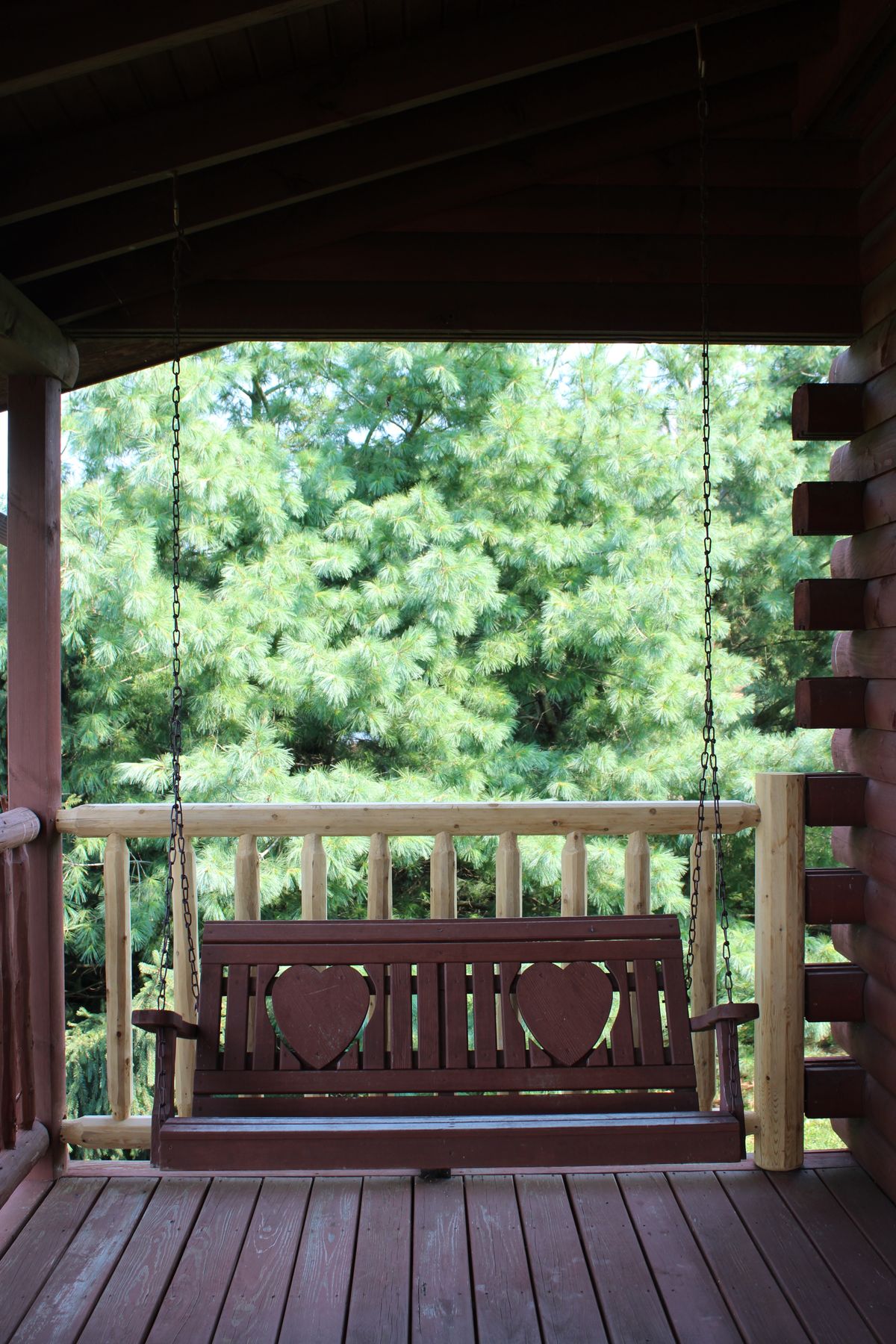 Charming wooden porch swing with heart design on rustic log cabin in Berlin, Ohio. Stock Photo.