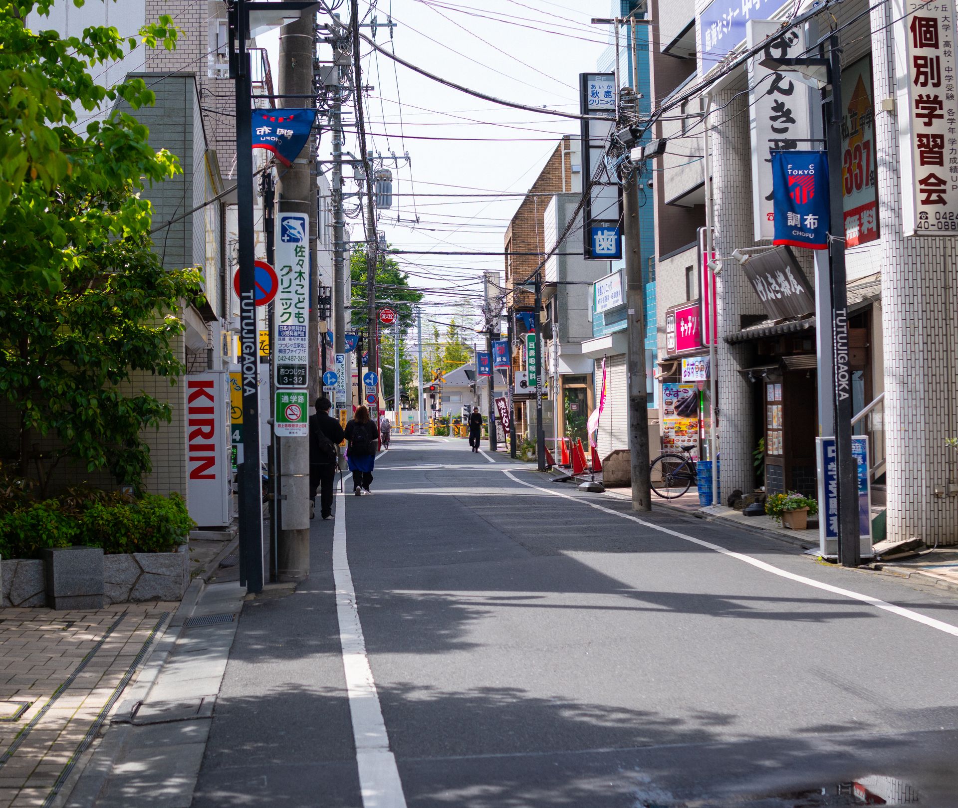 Street scene in Japan featuring power lines, signage, and pedestrians on a sunny day.