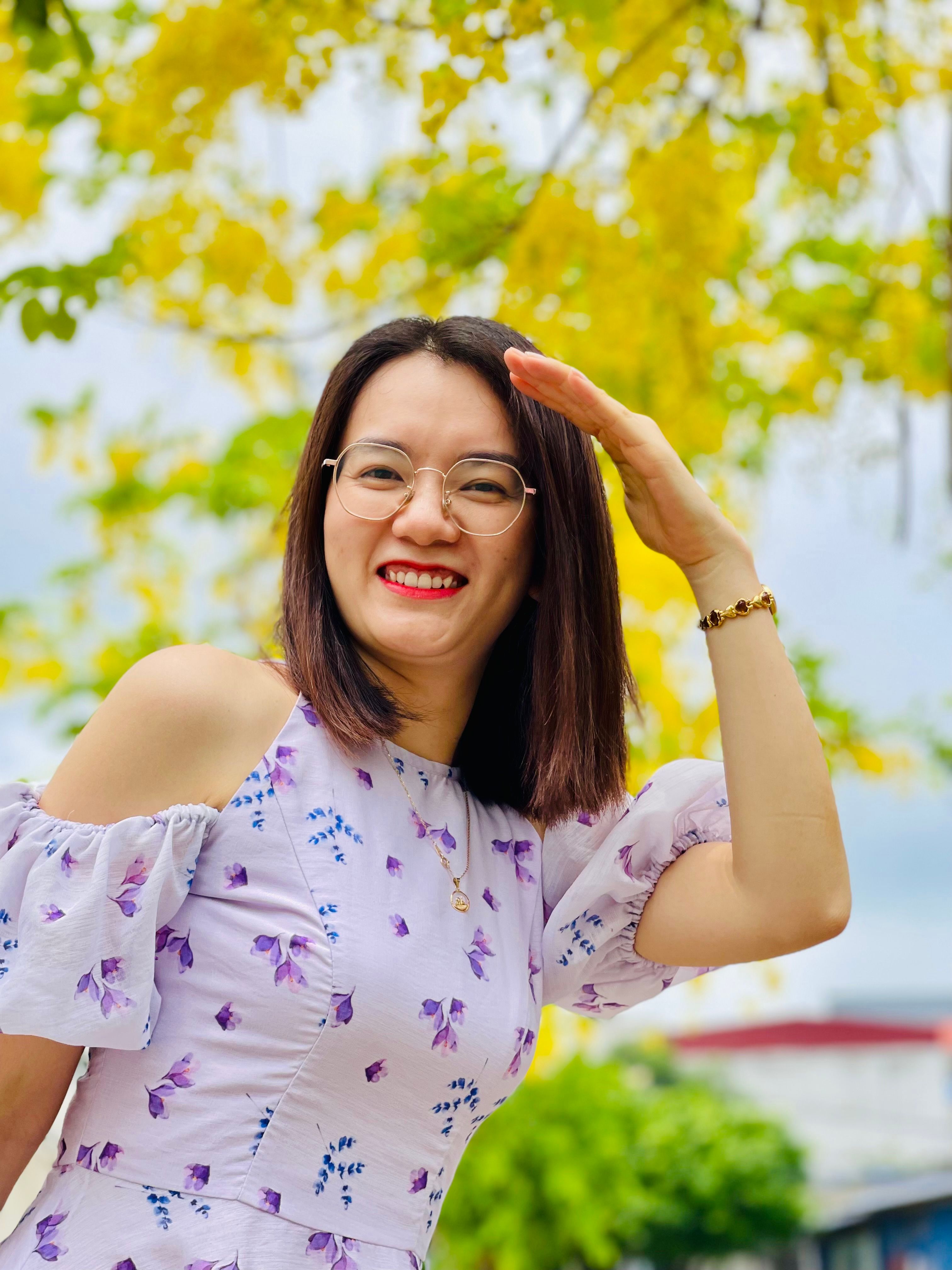 Cheerful woman posing under vibrant golden rain tree in Nam Định, Vietnam.