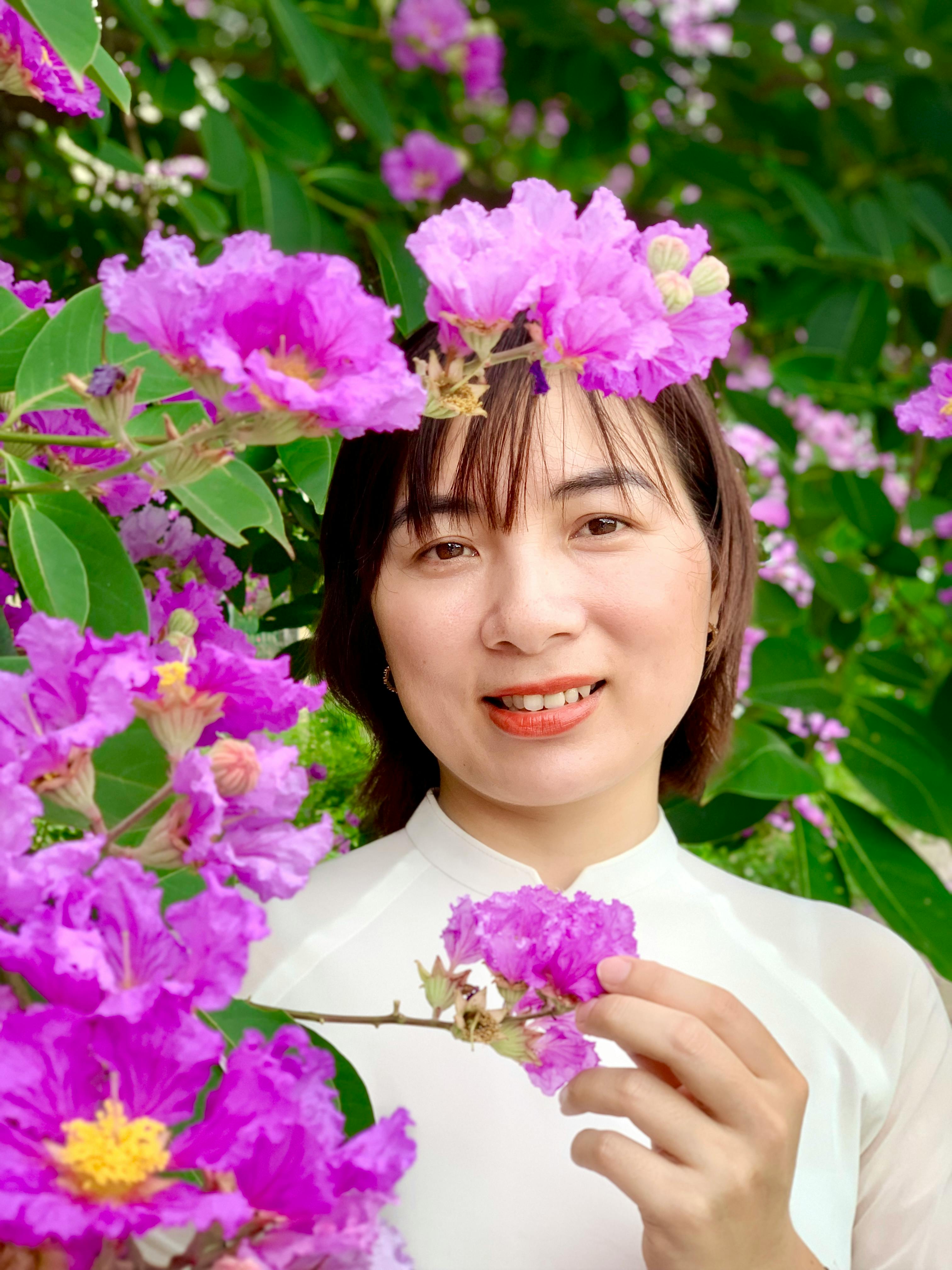 Woman in white dress surrounded by vibrant purple crape myrtle flowers in Nam Định, Vietnam.