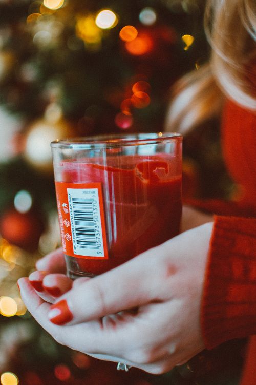 Free Warm holiday image of a red candle held in front of a decorated Christmas tree. Stock Photo
