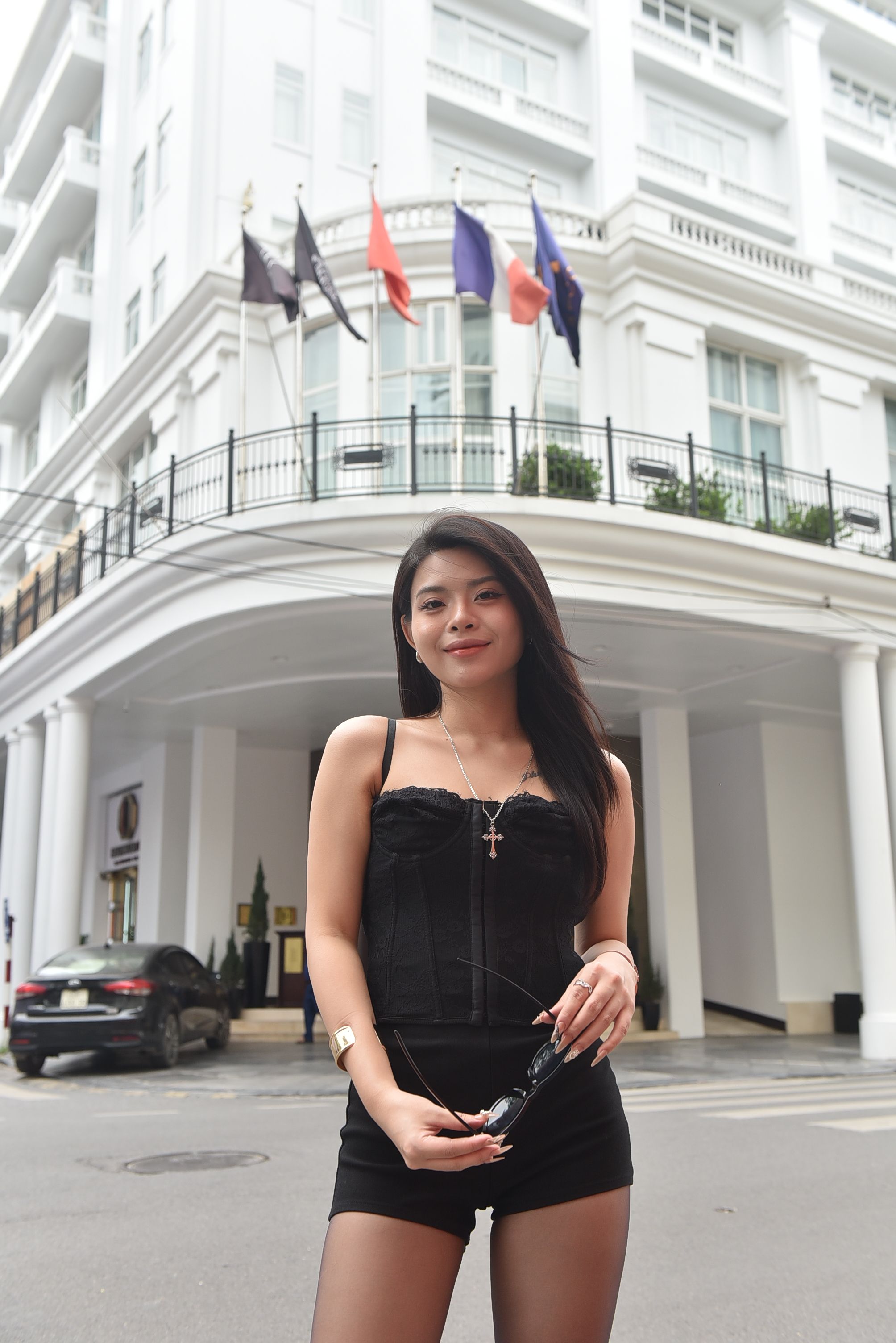 Young woman poses confidently in front of an elegant urban building facade with flags.