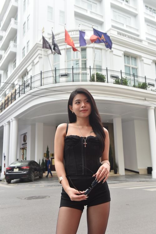 Free Elegant young woman in black outfit posing confidently in front of a luxury hotel entrance with flags displayed above. Stock Photo