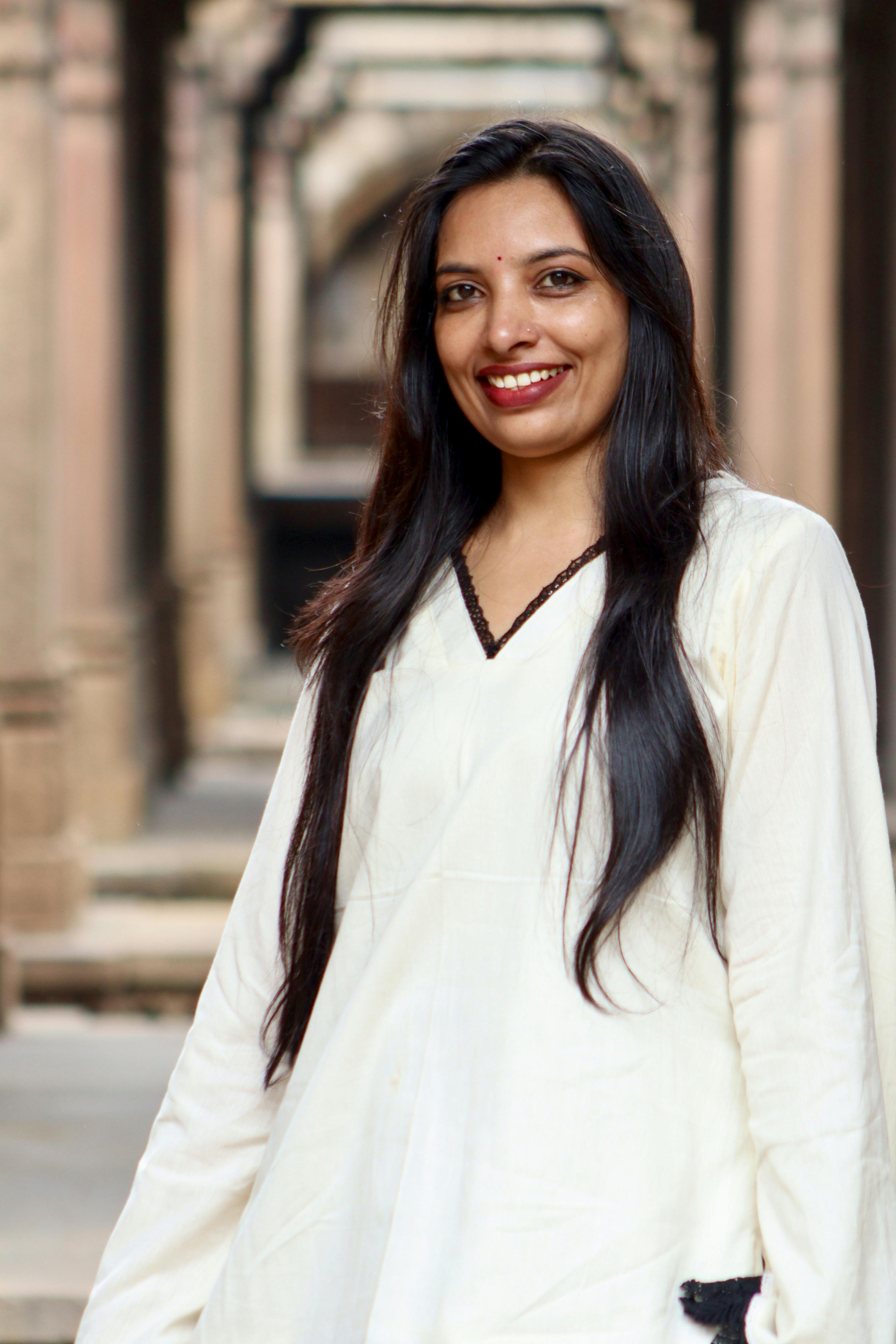 A woman in a white dress smiles warmly while standing in a historic architectural setting.