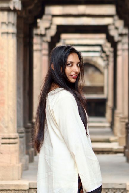 A young woman smiling while standing in a historical stone corridor adorned with intricate arches.