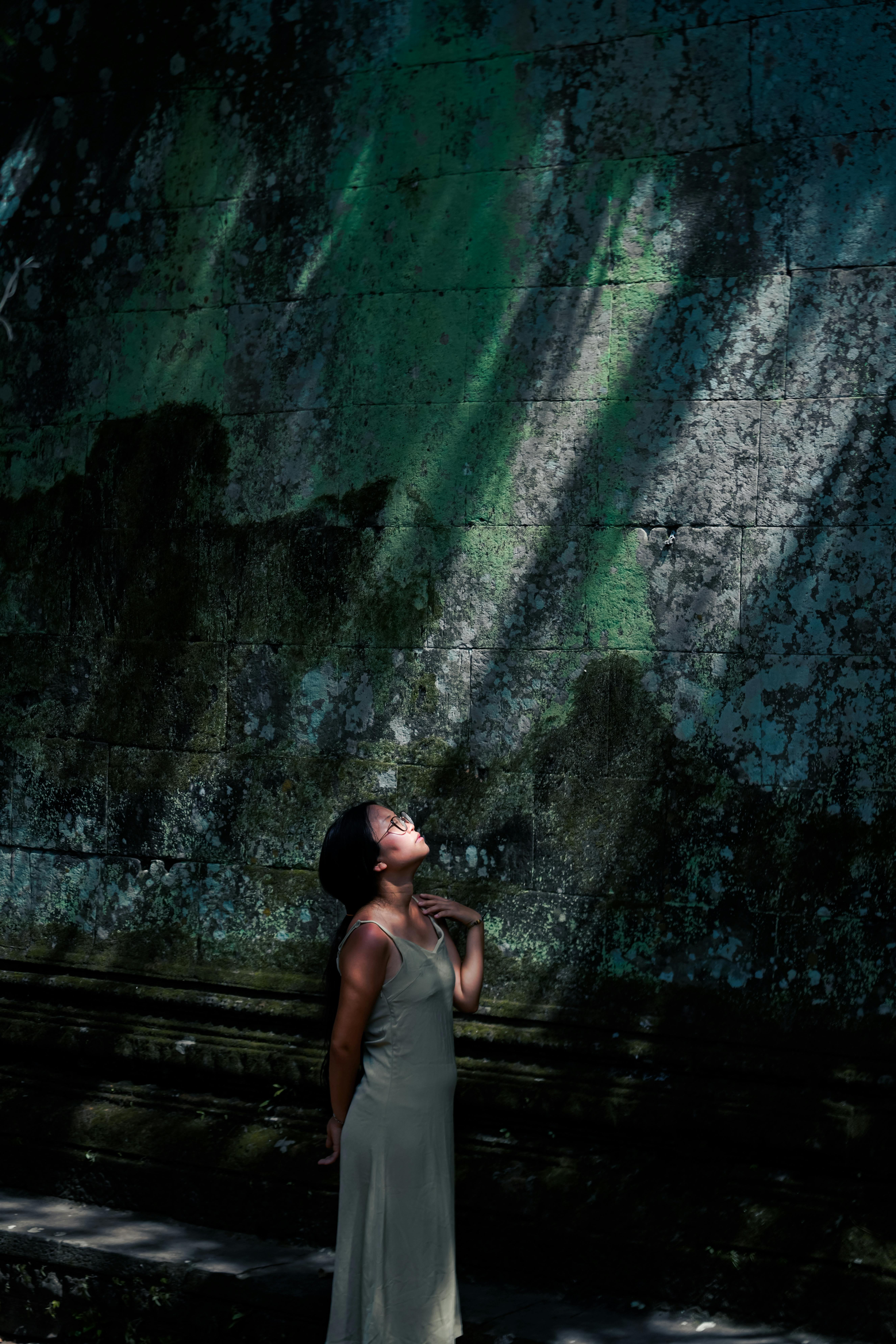 A woman basks in sunlight, casting shadows on a textured wall.