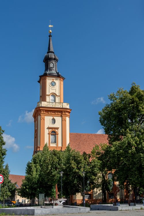 Free A stunning view of a historic Gothic church tower under a bright blue sky, surrounded by lush greenery. Stock Photo