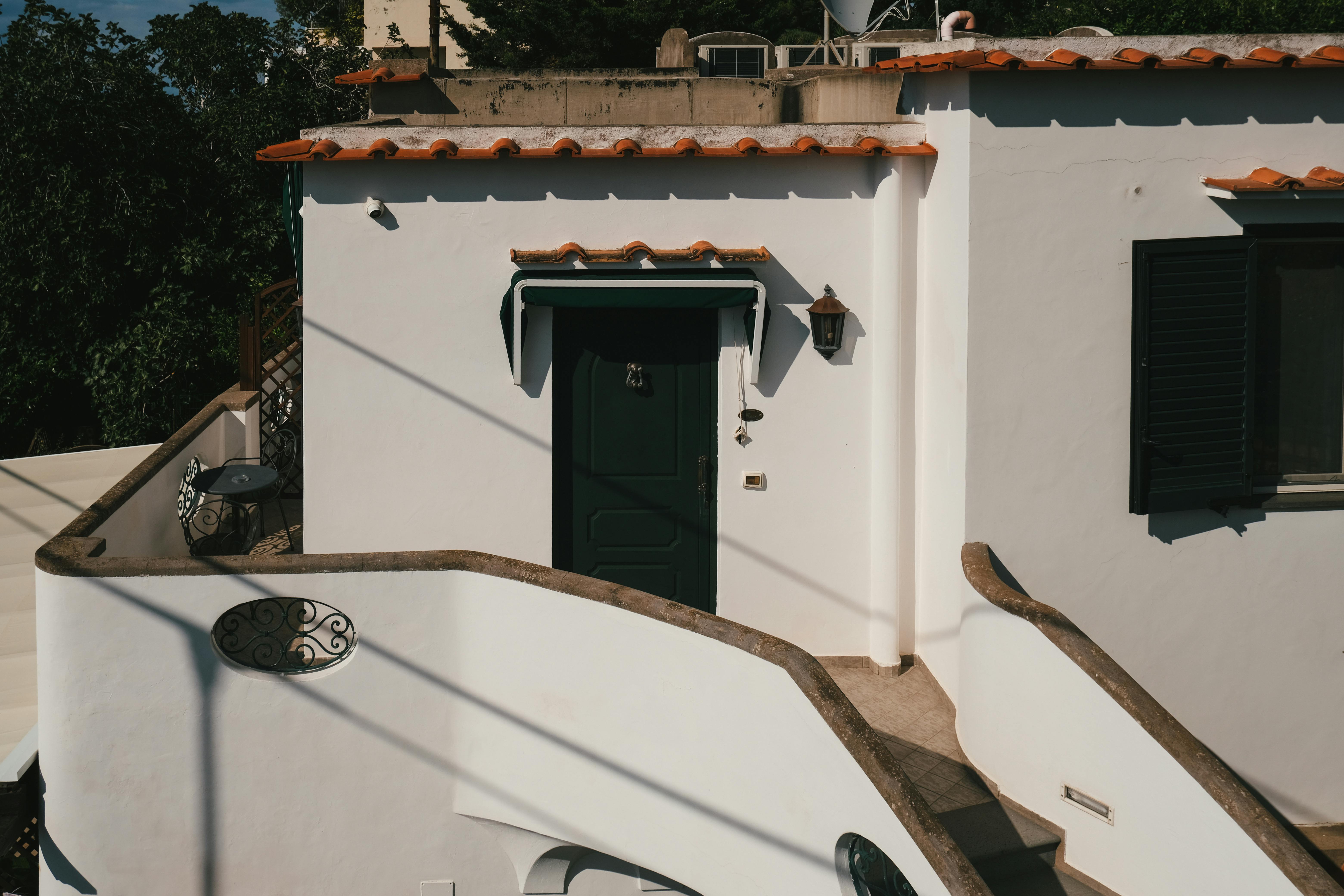 Charming Mediterranean-style house facade with distinct curved stucco staircase during a sunny day.