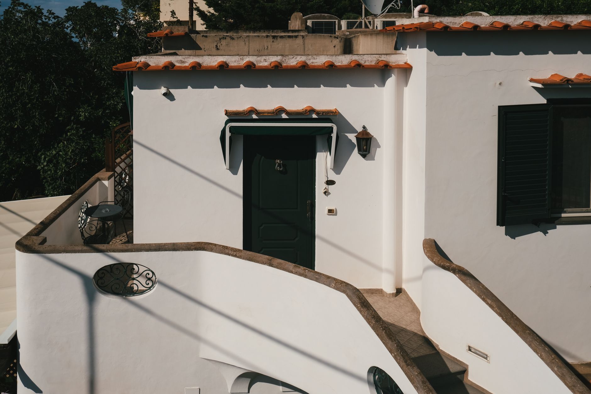 Cost To Paint A Stucco House Exterior In Minneapolis In 2026 2 Charming Mediterranean-style house facade with distinct curved stucco staircase during a sunny day.
