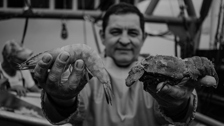 Black and white image of a fisherman showcasing fresh shrimp and lobster on a boat.