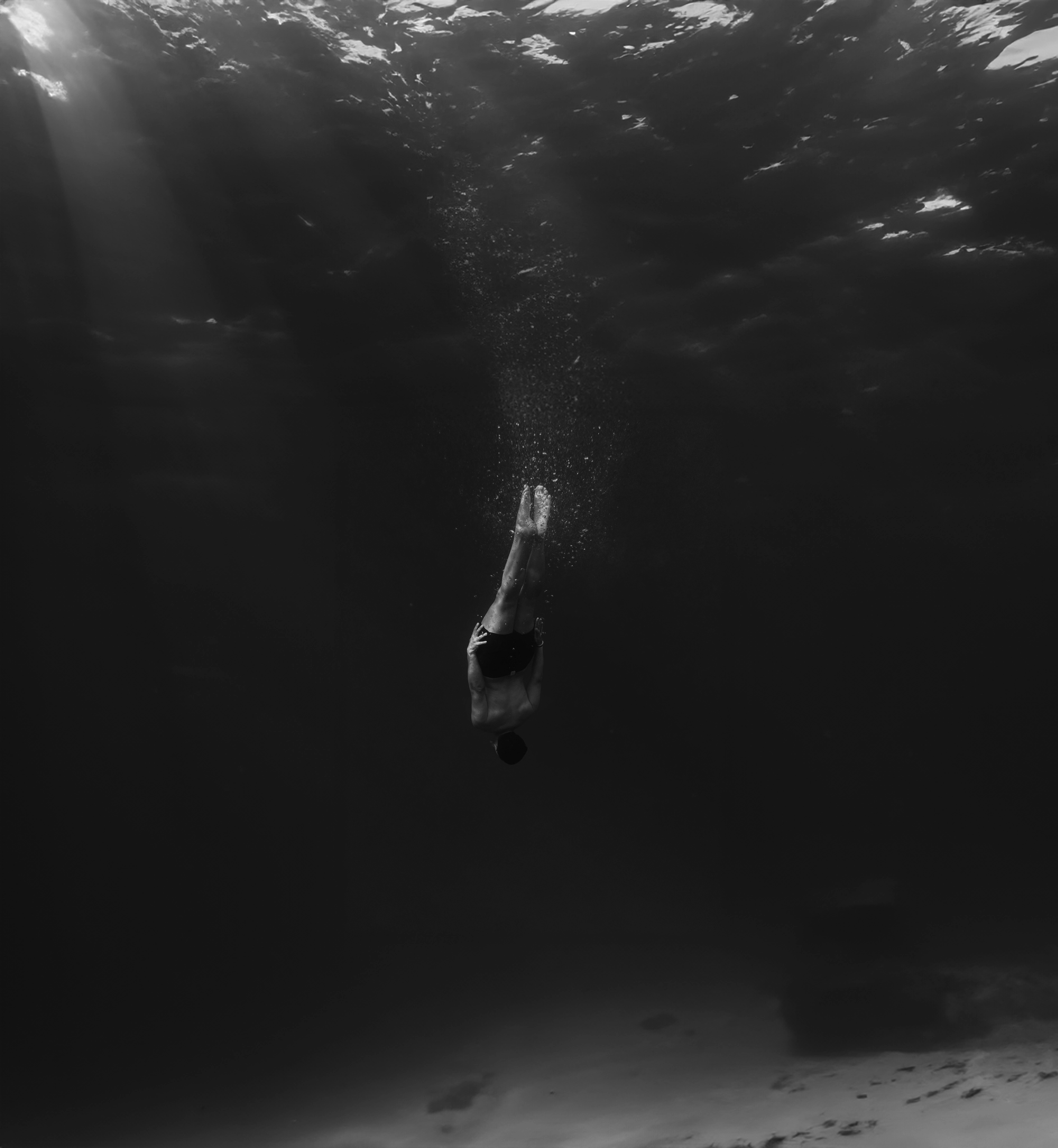 A lone diver gracefully descends into the deep ocean, creating a dramatic black and white underwater scene.