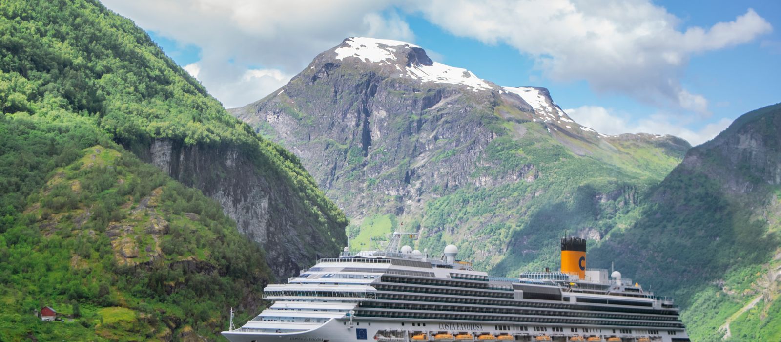 A large cruise ship at anchor in Geirangerfjord below green mountain slopes.