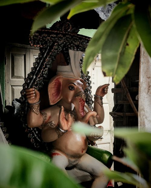 Free Explore the beauty of a detailed Ganesh idol surrounded by green foliage, capturing a spiritual essence. Stock Photo
