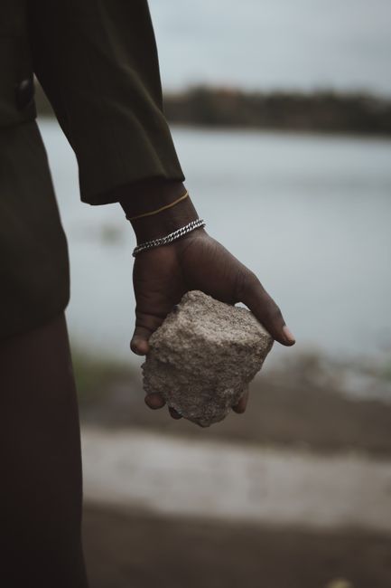 Fotomural Una mano adulta sosteniendo una roca cerca de la orilla de un lago, centrándose en las texturas.