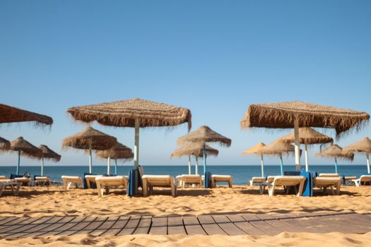 Peaceful beach scene with straw umbrellas and deck chairs on a sunny day.