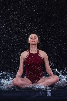 Woman meditating with water splash against black background, creating a dynamic, serene atmosphere.