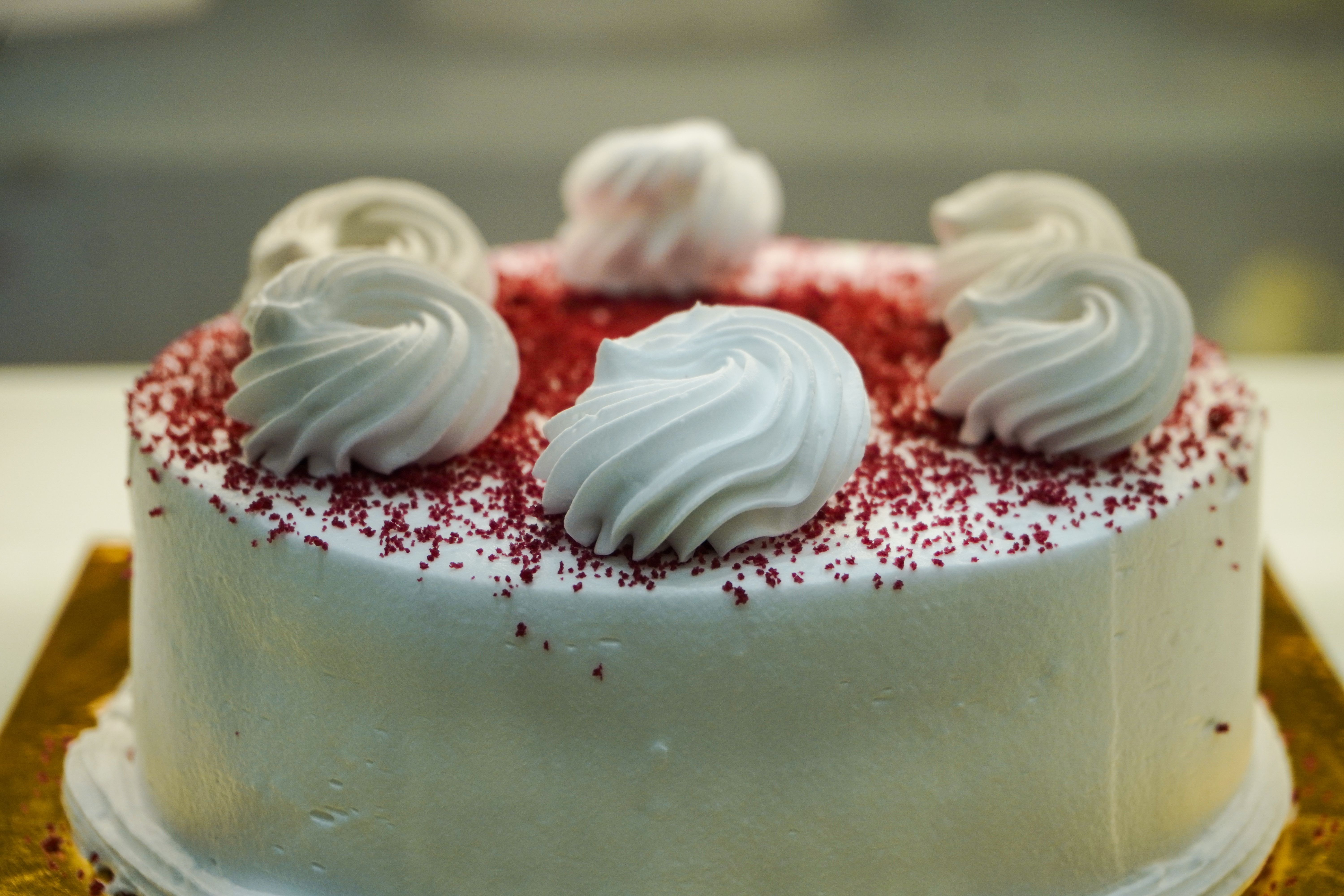 A cream-frosted cake piped with rosettes and dusted with red crumb.