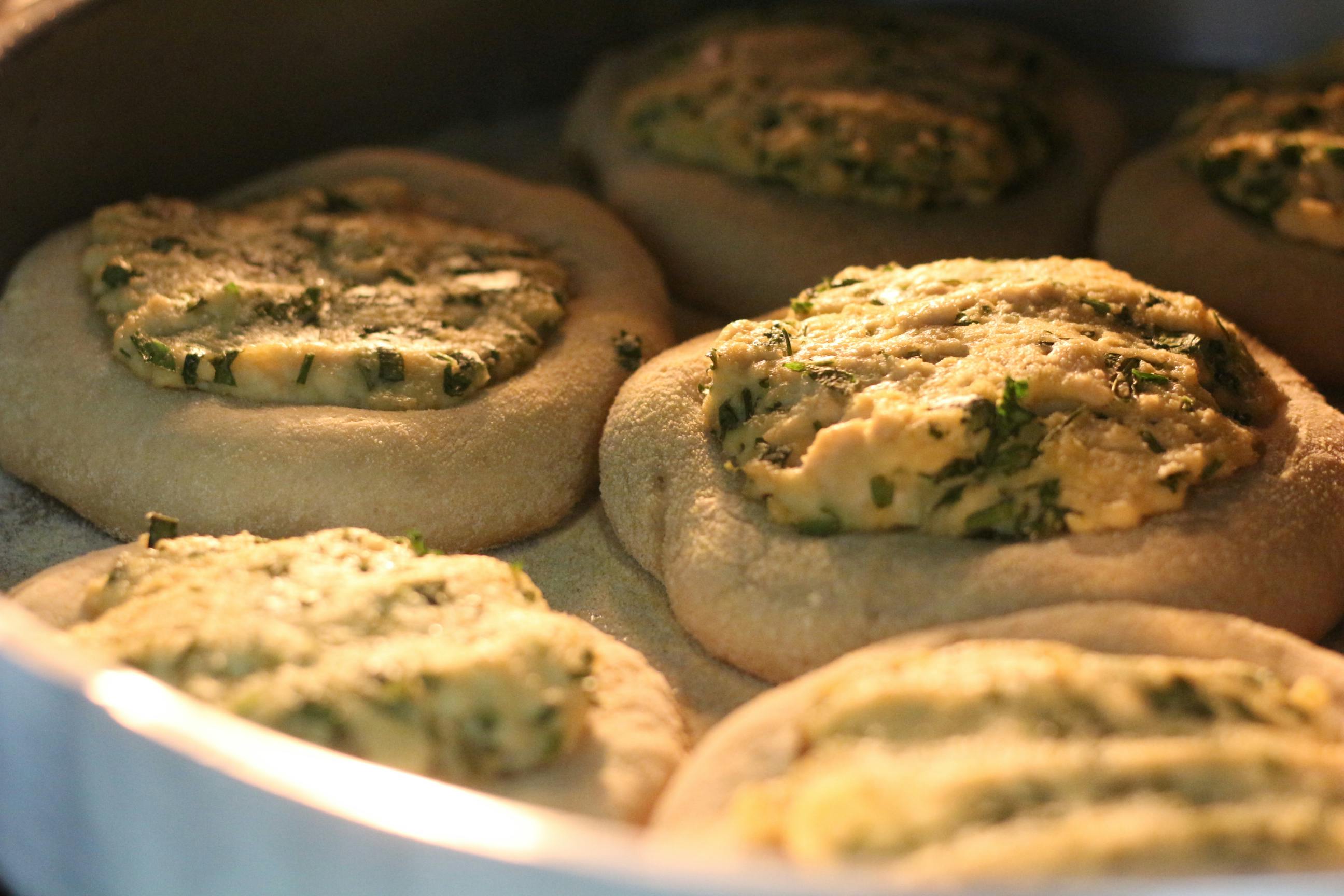 Golden esfiha topped with herbs and tofu baking in oven, showcasing vegan cuisine.