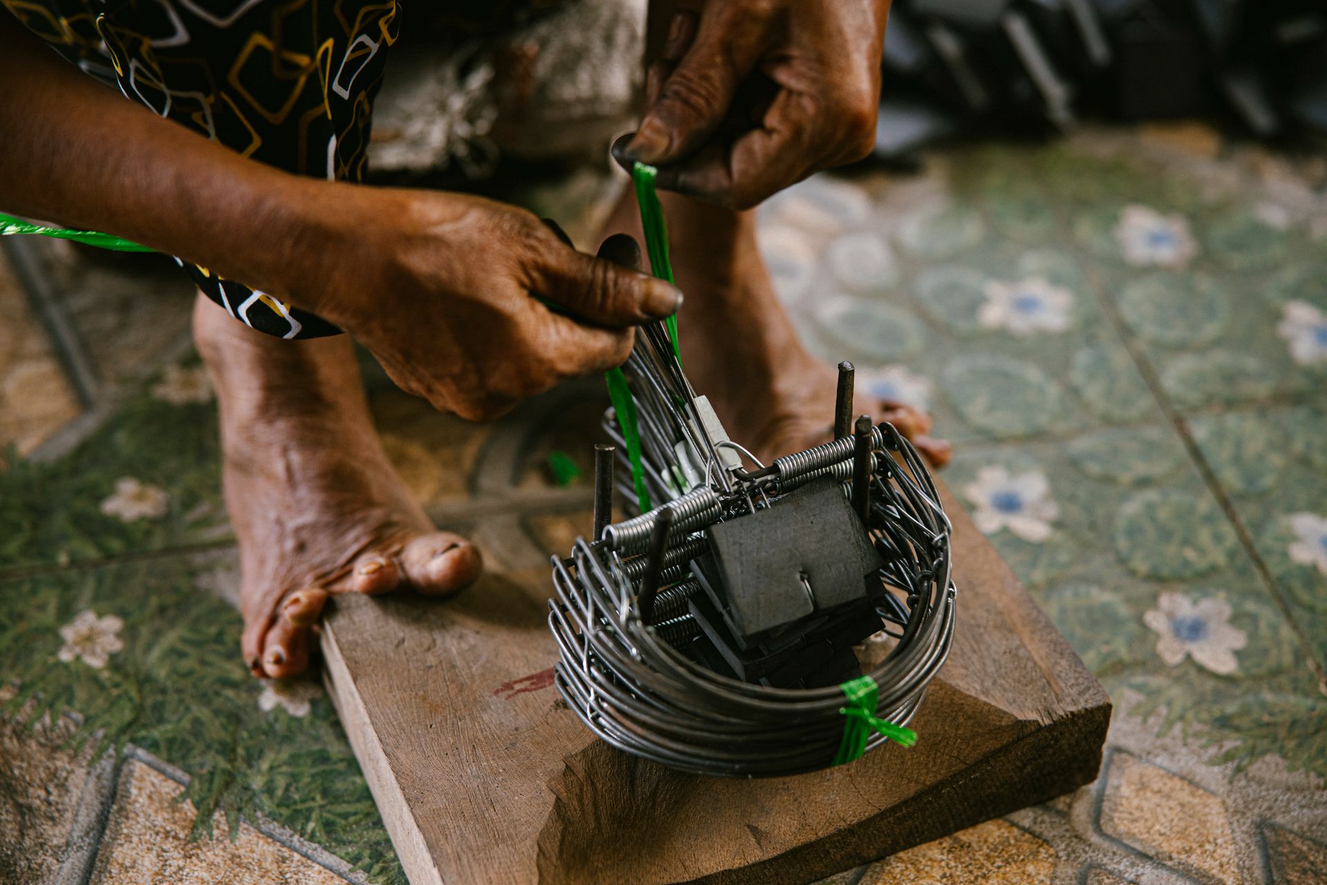 Craftsman's hands skillfully weaving a metal trap on wooden base indoors. Traditional craftsmanship.