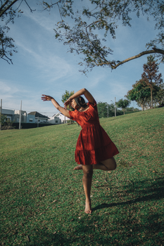 A young woman in a red dress dancing in a sunny green park, expressing freedom.