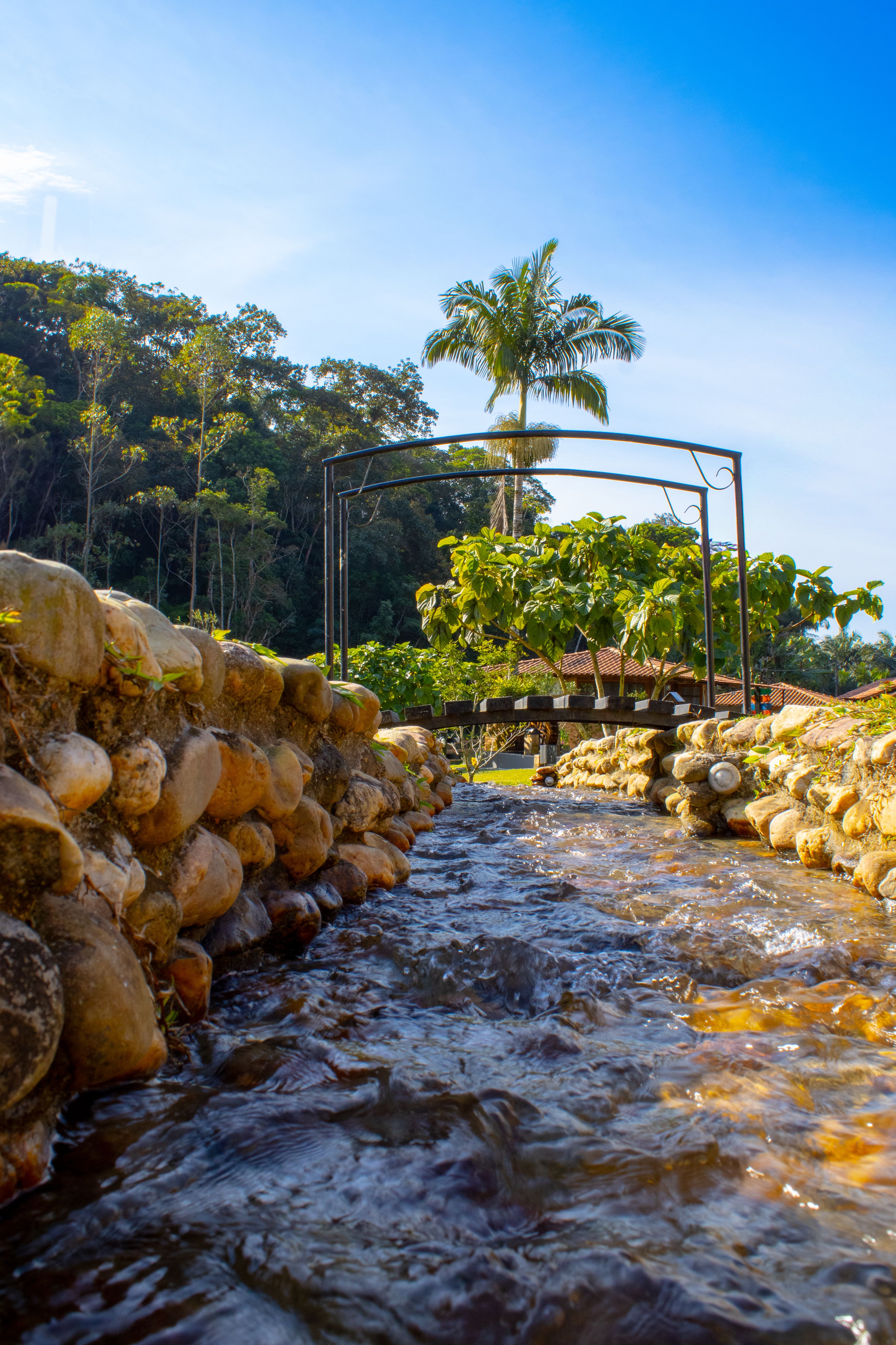 Tranquil stream with stone banks and lush vegetation in Gaspar, Brazil under a clear sky.