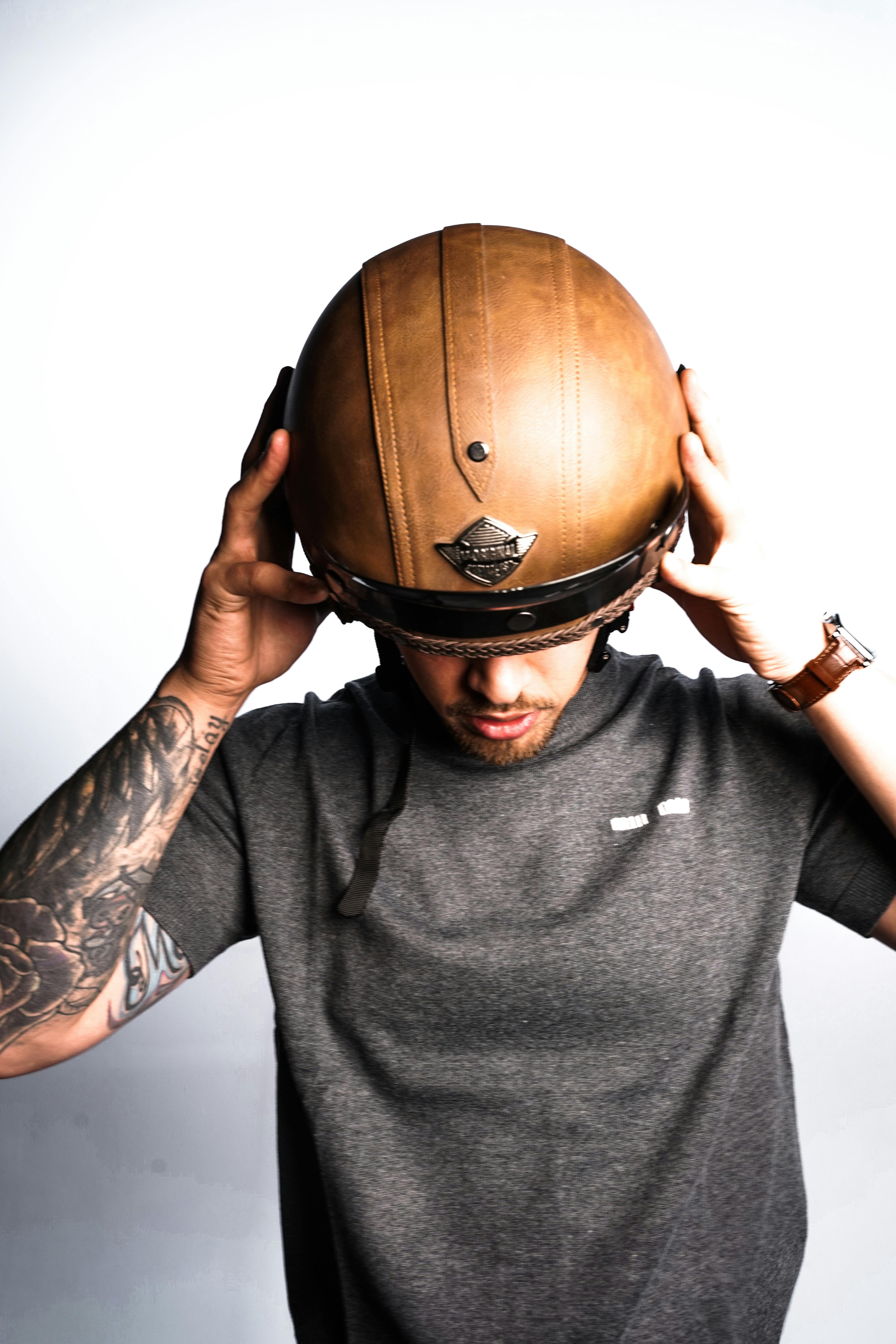 Tattooed man wearing a vintage leather motorcycle helmet. Studio shot with minimalist background.