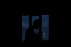 Moody silhouette of a person framed by a window with a dark, twilight sky in the background.