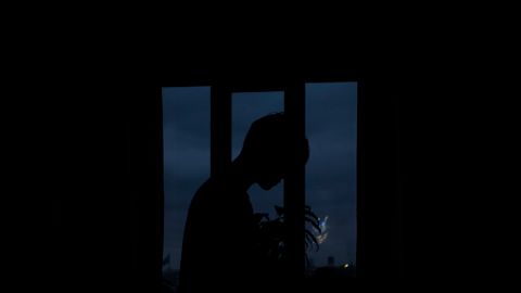 Moody silhouette of a person framed by a window with a dark, twilight sky in the background.