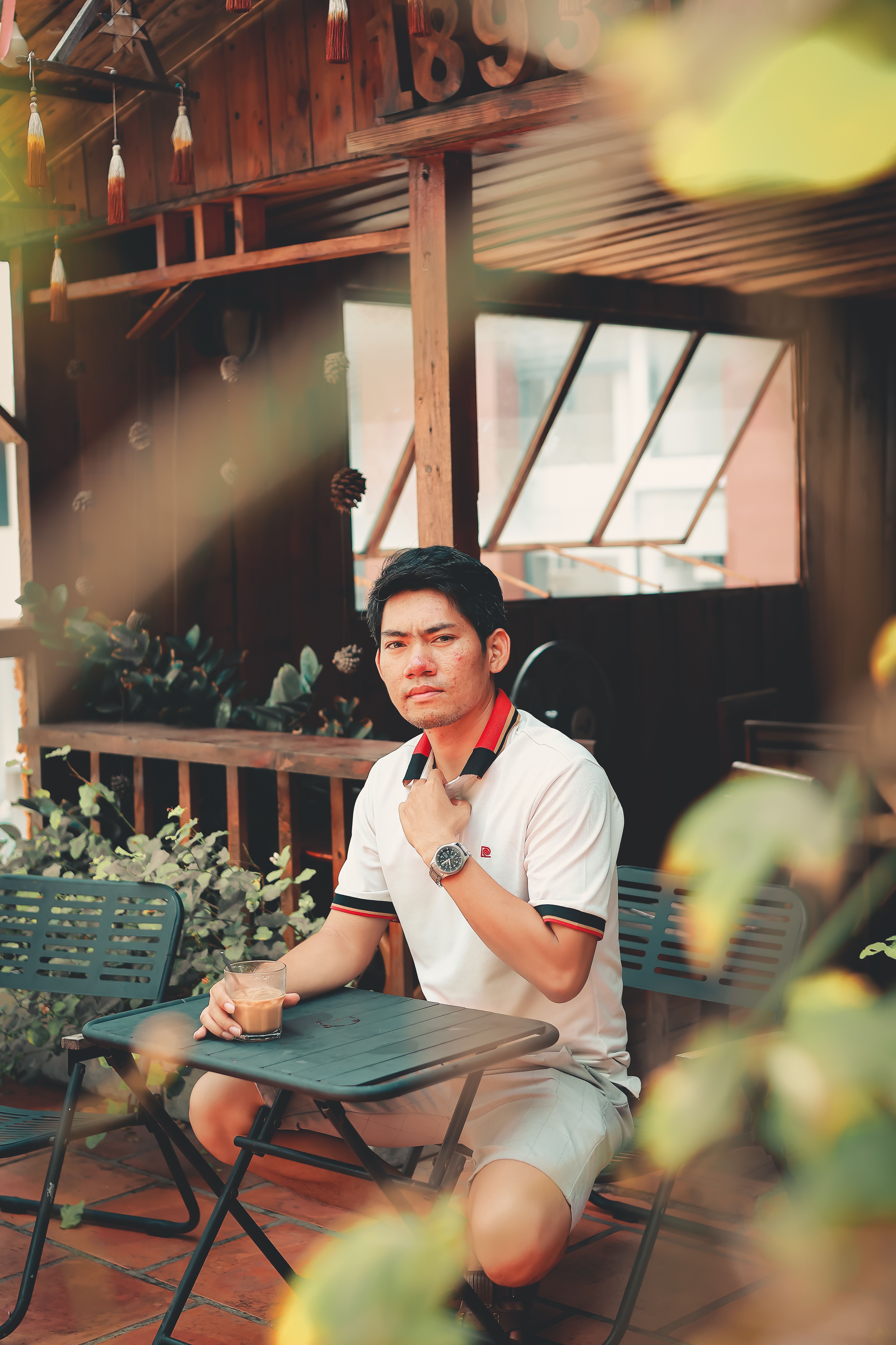 Man sits outdoors enjoying a refreshing drink under warm sunlight at a cafe.