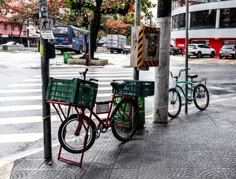 A rainy street corner in Santos, São Paulo with parked bicycles and traffic in the background.