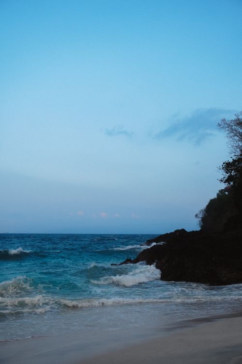 Free A tranquil scene of a Bali beach with gentle waves under a twilight sky. Stock Photo