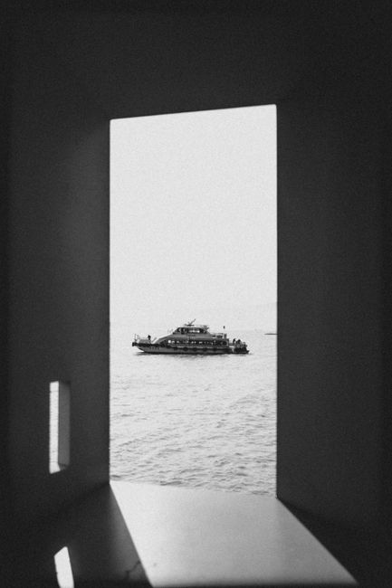 A boat quietly sails on the sea, viewed through a window, creating a peaceful scene.