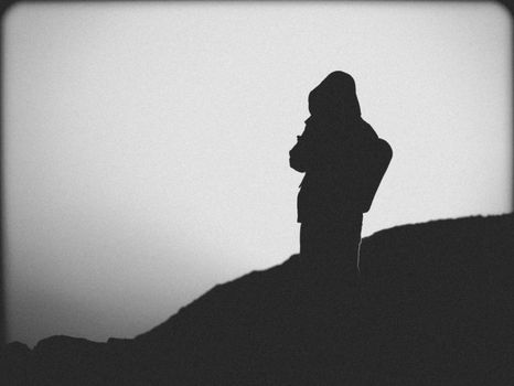 Dramatic black and white silhouette of a person on a hillside during twilight. Perfect for conceptual and artistic themes.