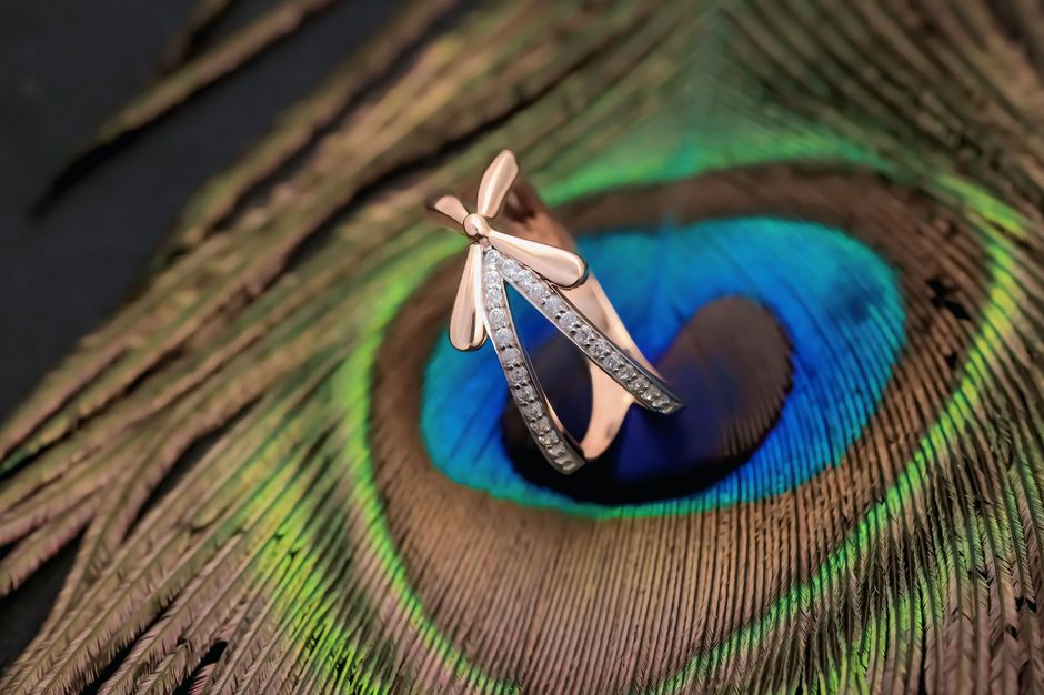Rose gold ring with diamonds elegantly displayed on a vivid peacock feather for a luxurious touch.