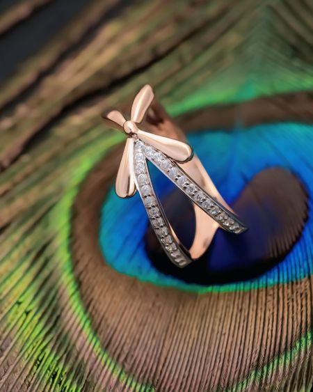 Rose-gold ring with a sparkling zircon band resting on a peacock feather
