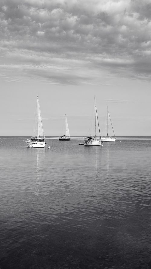 Free Four sailboats calmly anchored under a textured sky, reflecting peace and solitude. Stock Photo