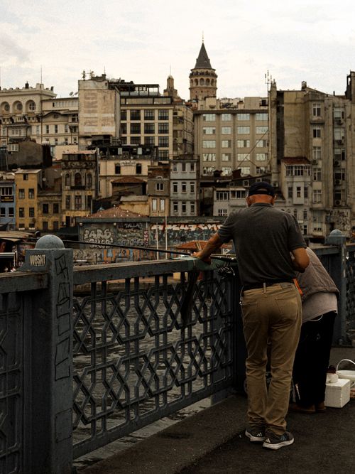 Free Two people fishing on Galata Bridge overlooking historic Istanbul cityscape. Stock Photo