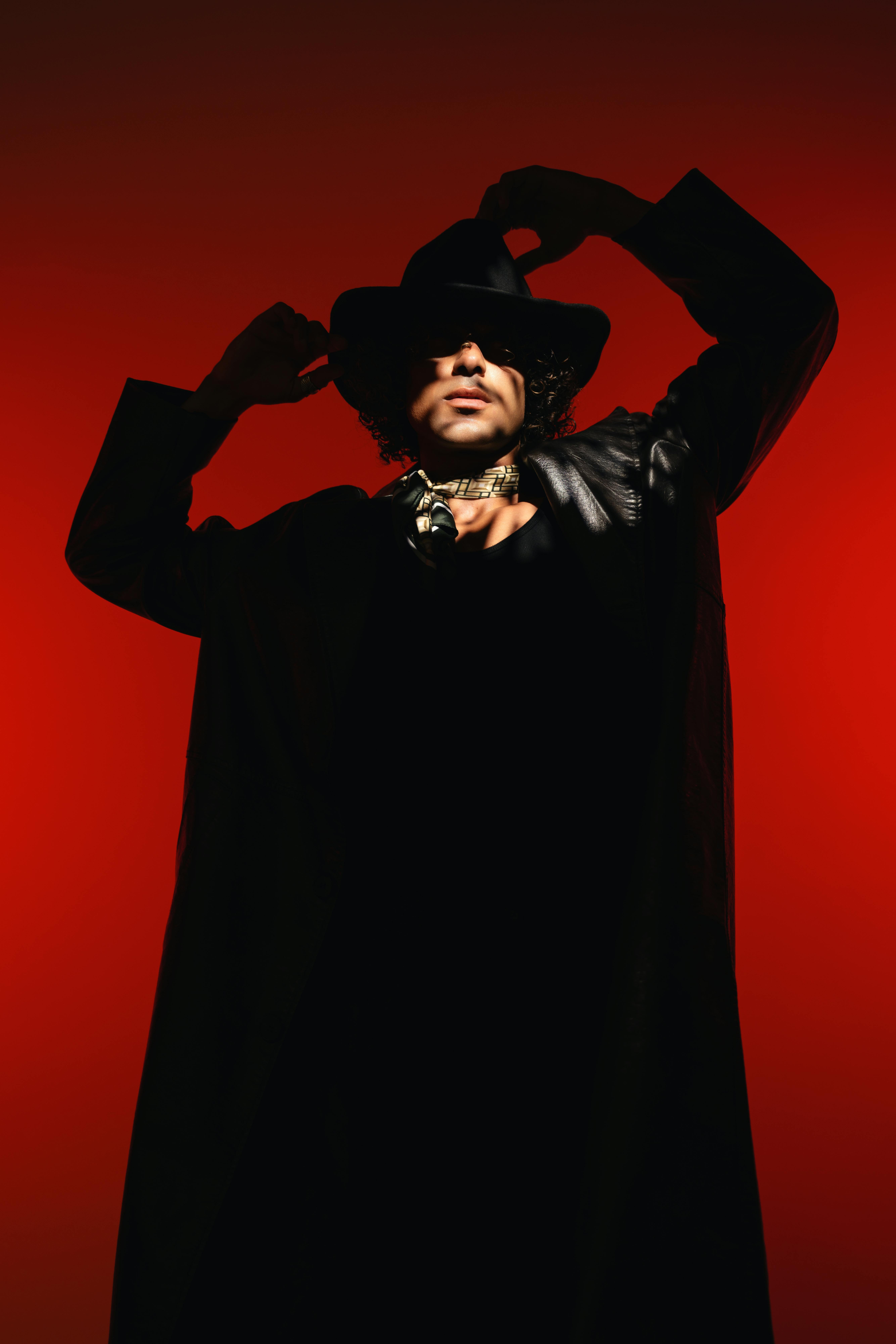 Avant-garde portrait of a stylish man in a hat against a red background.